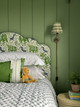 Bedroom with green panelled walls and a classic La Jungle green upholstered headboard featuring jungle animals in a Raoul Dufy–inspired print. Bed dressed with cushions and quilt. Side view detail. Room designed by Kit & Co.